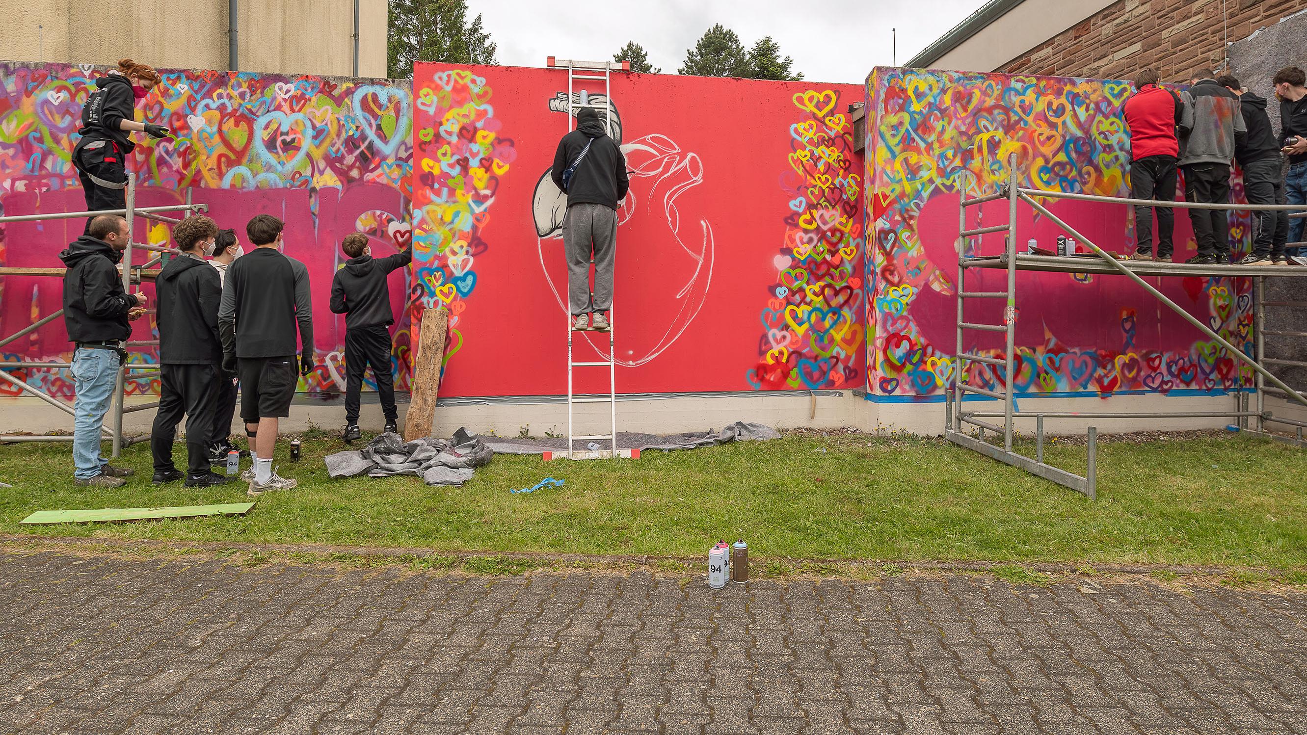 Mit Spraydosen sprühen die Jugendlichen ein zuvor gestaltetes Graffiti an die Mauern rund um die Jugendkirche MIA in Rappweiler.